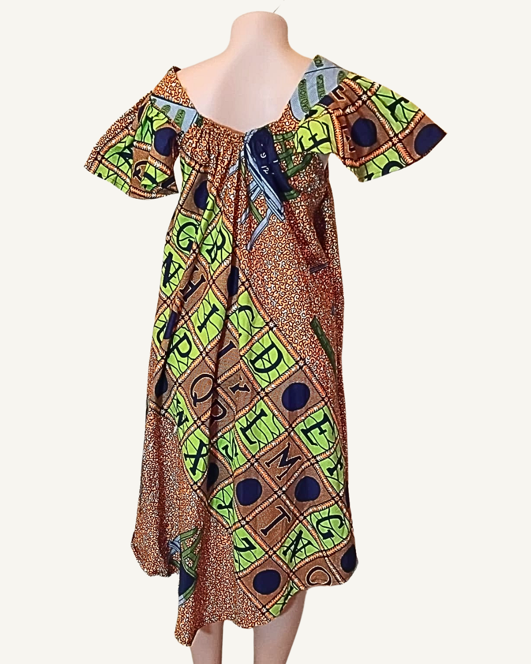 Vue dos · robe wax patchwork caramel et vert anis · composition diagonale bien visible · col bardot froncé avec petit nœud central · manches papillon évasées · coupe trapèze ample · ourlet asymétrique plus long sur les côtés.