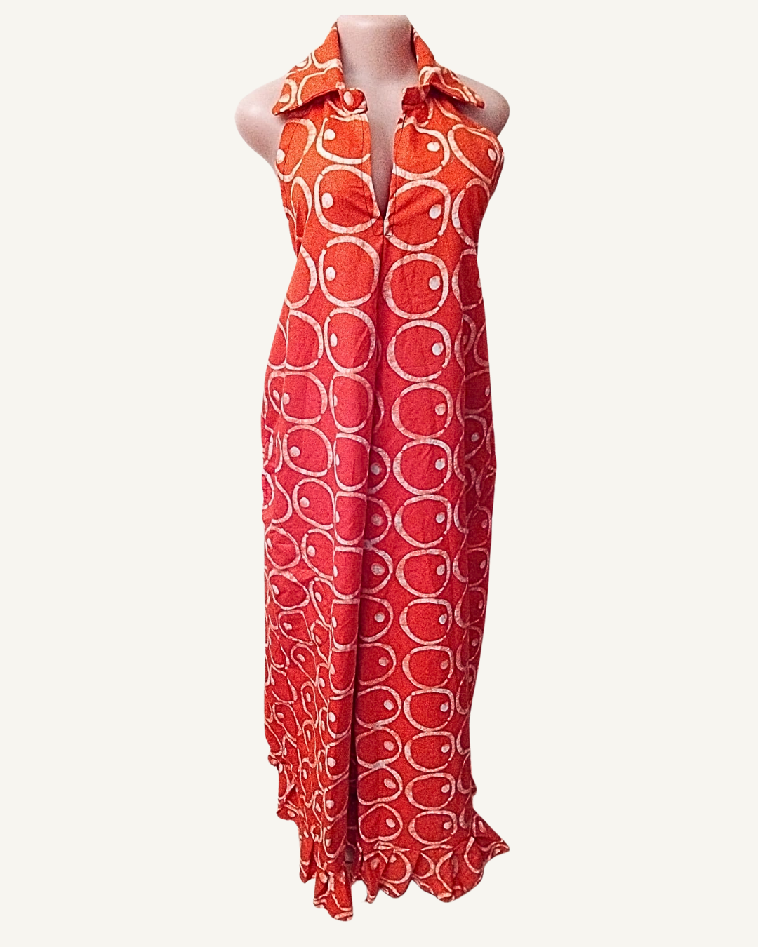 Robe longue batik africain rouge corail à rouge vif, col chemise retourné, encolure V profonde, sans manches, motifs ovales et cercles blancs sur toute la surface, ourlet volant froncé.