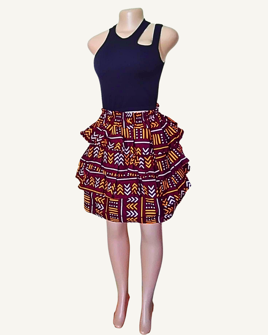 Jupe courte à trois volants étagés froncés en bogolan bordeaux · flèches et chevrons orange et blanc · taille élastiquée · longueur genou · portée avec crop top noir (couleur non choisissable à la commande).