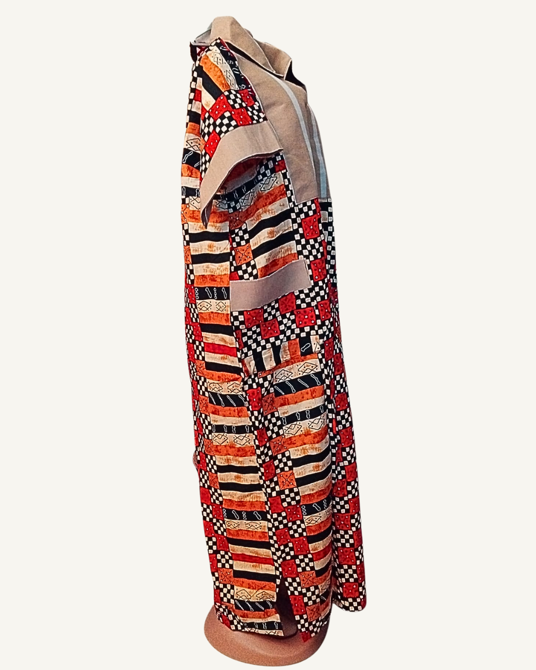 Vue de profil — robe longue batik africain patchwork rouge noir et orange, empiècement beige lin avec col chemise et zip central, manche courte batik à revers beige, poche plaquée beige visible sur le côté, coupe droite ample longueur cheville.