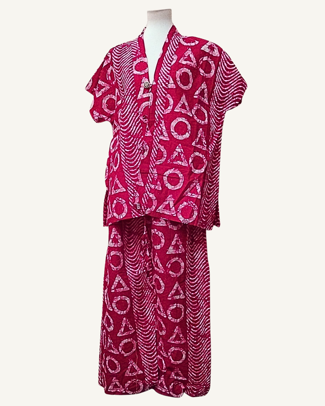 Ensemble 2 pièces batik africain fuchsia profond, veste kimono courte ouverte col V croisé avec bouton doré central, manches courtes tombantes, motifs cercles et triangles rose et blanc sur fond de vagues concentriques, pantalon palazzo taille élastiquée larges jambes longueur cheville même tissu.