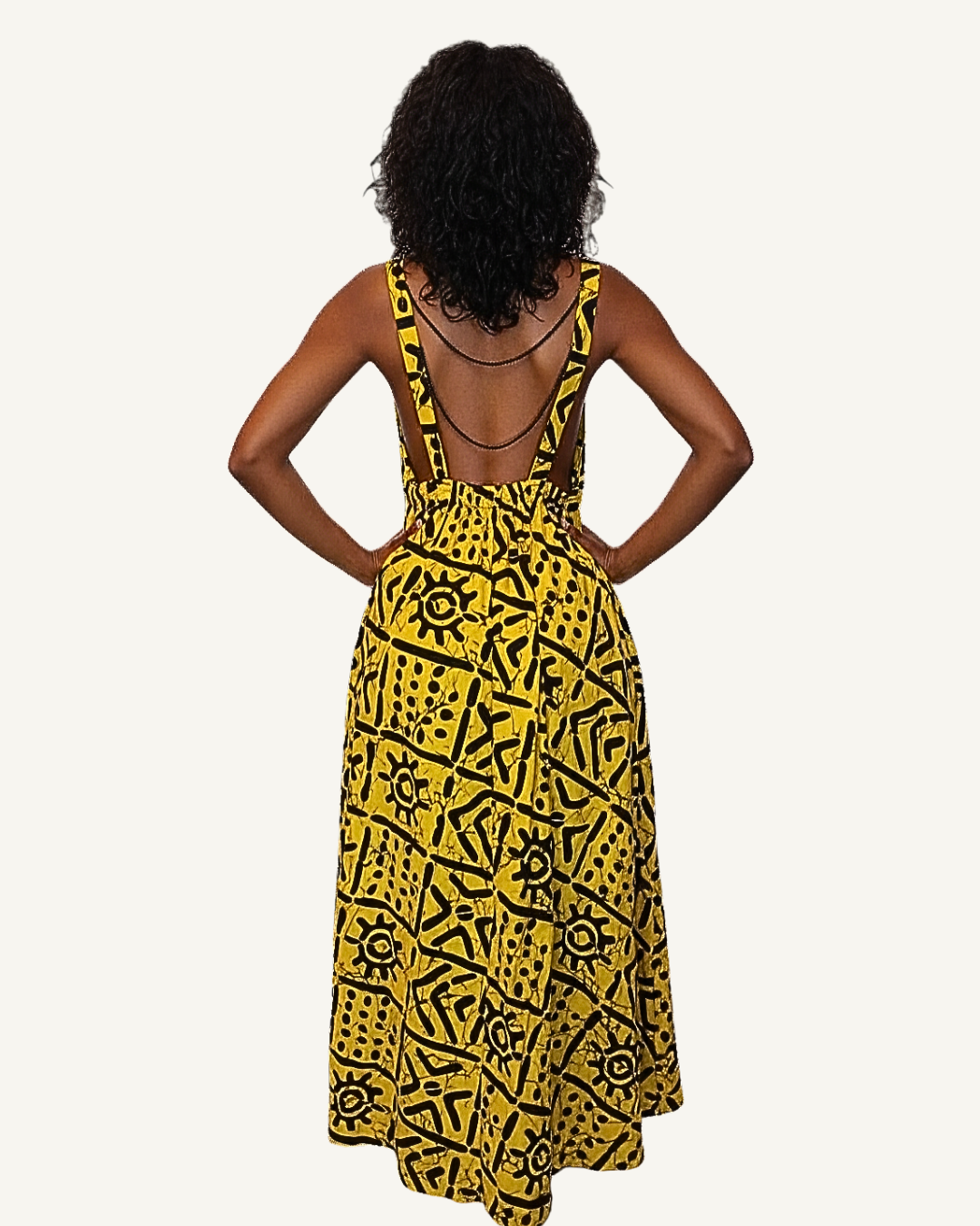 Vue dos · robe batik jaune · dos entièrement nu · bretelles larges qui se rejoignent à la taille froncée élastiquée · jupe évasée ample · symboles noirs sur fond jaune vif · longueur cheville.