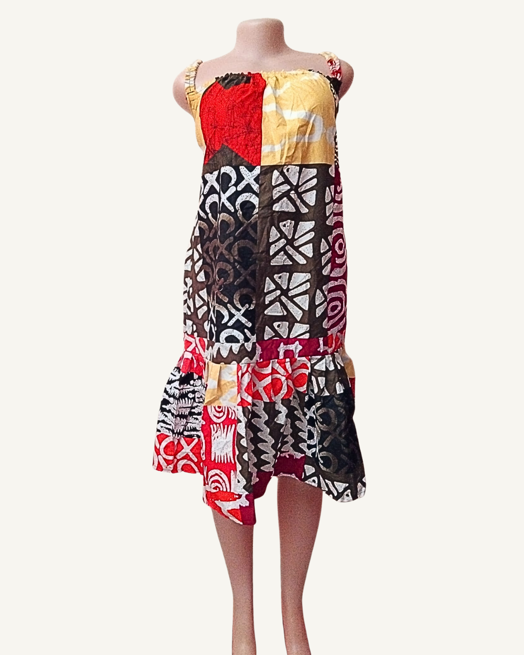 Robe courte batik africain patchwork, blocs de tissus rouge, marron, jaune doré et bordeaux, motifs géométriques et tribaux variés, bretelles froncées élastiquées, froncé sous poitrine, volant asymétrique genou.