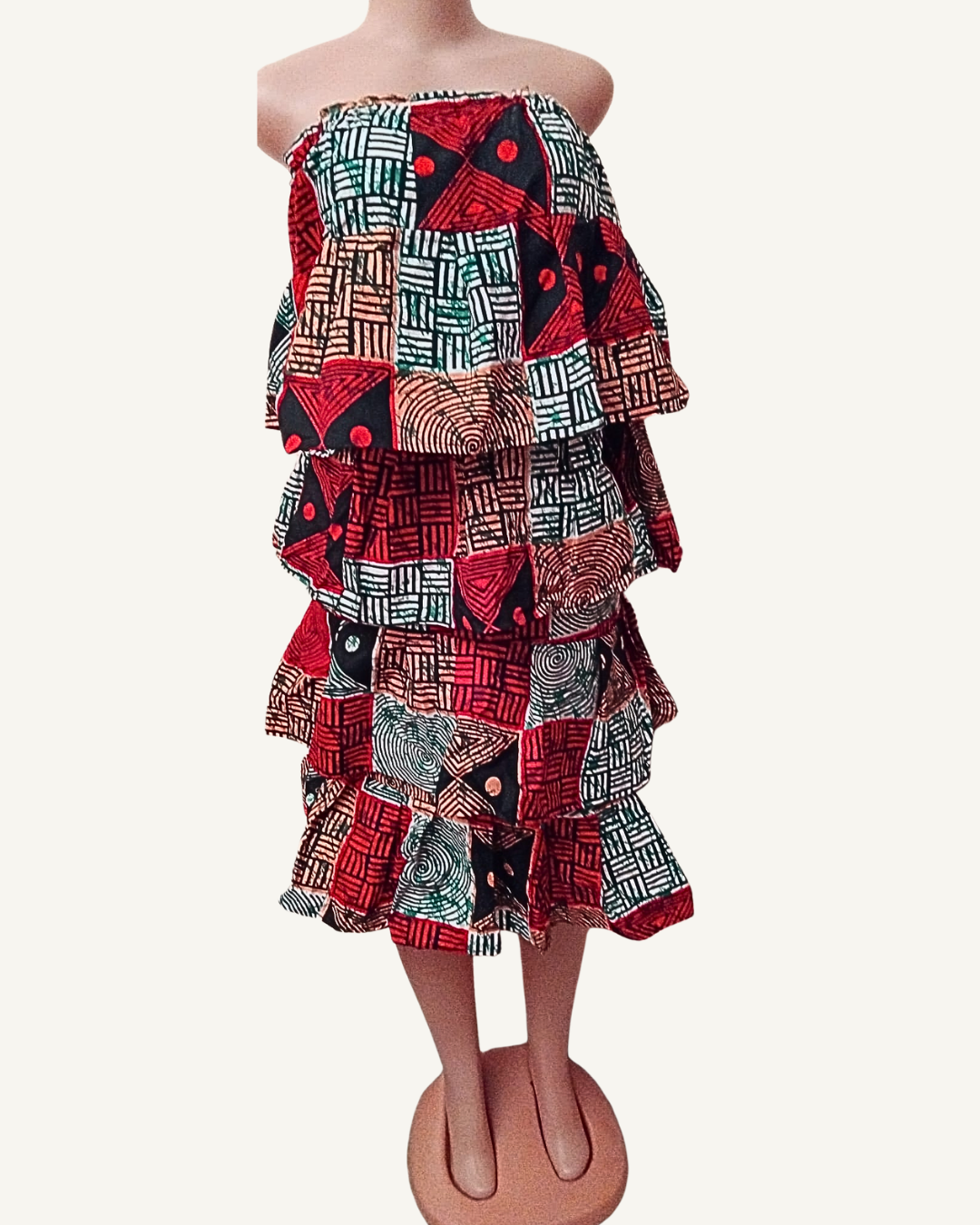 Robe bustier courte en wax africain rouge, noir et vert, quatre volants étagés superposés du buste au genou, motifs géométriques mêlant hachures, triangles et spirales, buste smocké élastiqué.