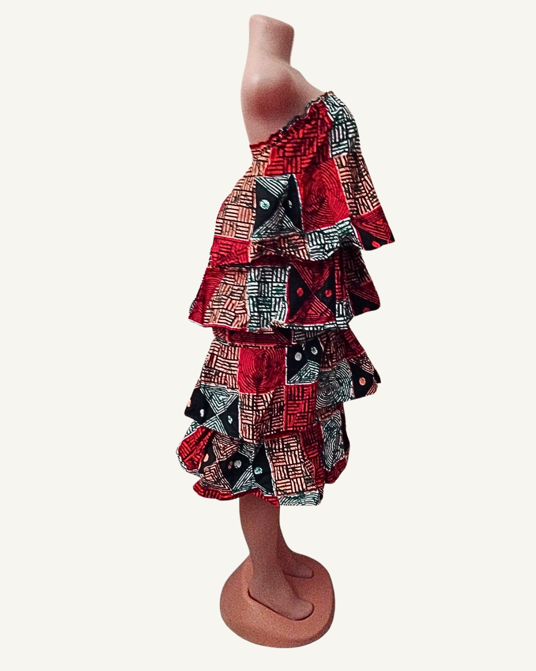 Vue de profil — structure en cascade des quatre volants étagés bien visible, amplitude et volume de chaque rang, longueur genou, wax africain multicolore.
