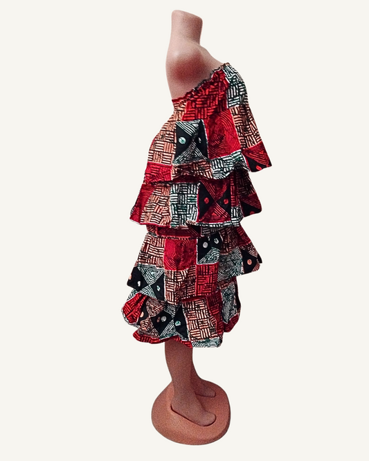 Vue de profil — structure en cascade des quatre volants étagés bien visible, amplitude et volume de chaque rang, longueur genou, wax africain multicolore.