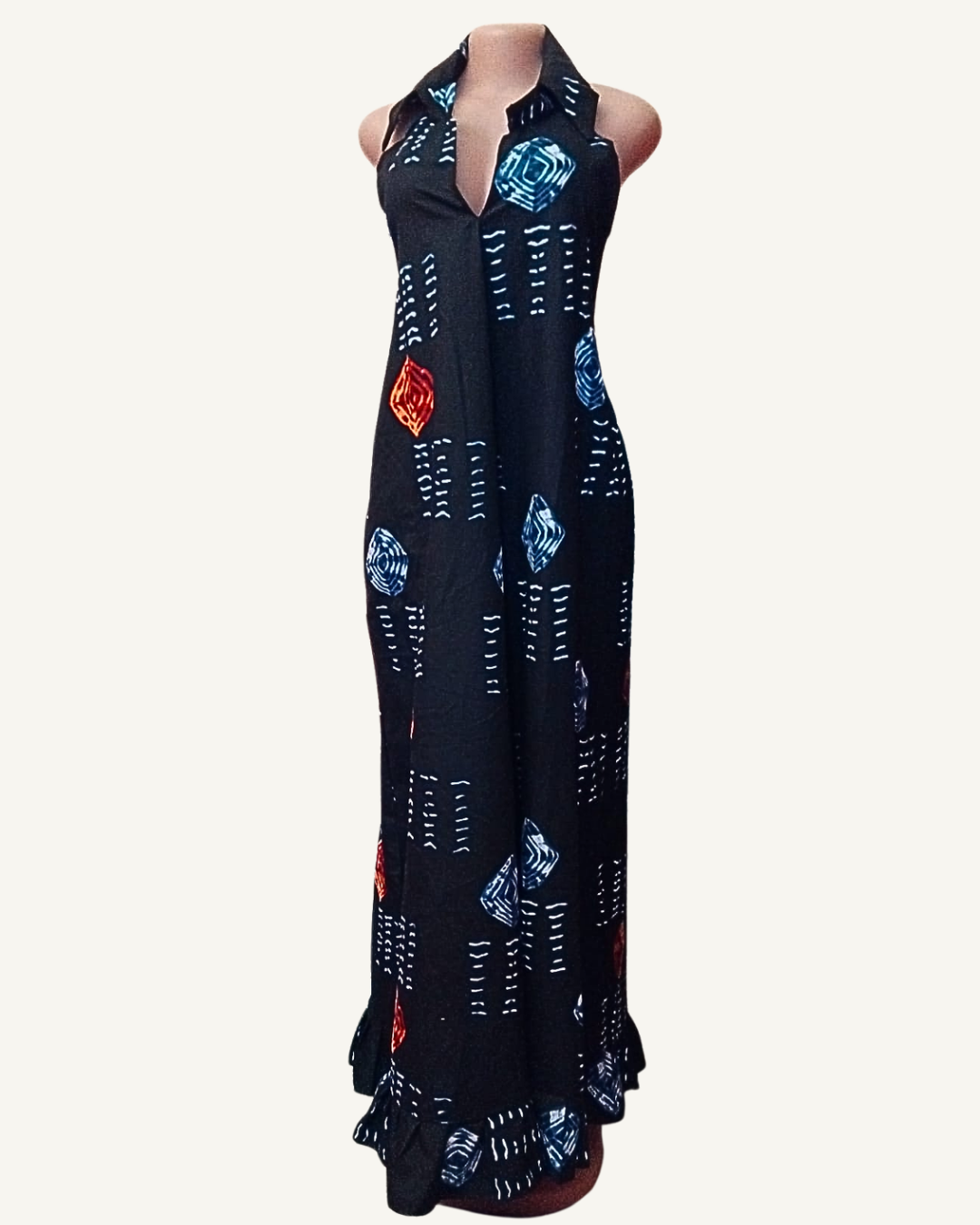 Vue face — robe maxi adire noir, col chemise retourné, ouverture V profonde, sans manches, losanges concentriques bleu indigo et rouge orangé sur fond noir, tirets blancs en lignes horizontales, ourlet volant froncé.