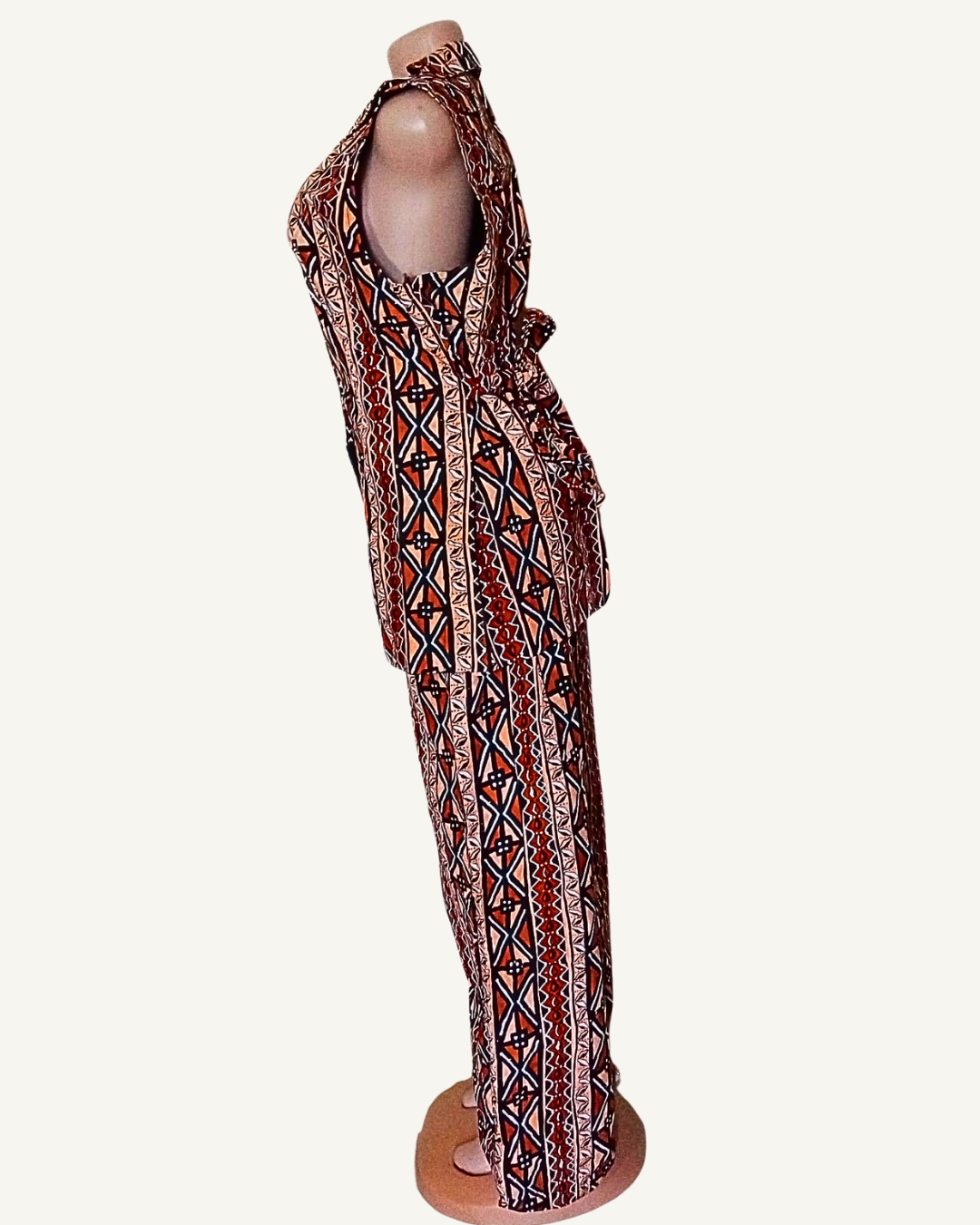 Vue de profil · ensemble wax africain terracotta et sable · blazer sans manches col retourné cintré · pantalon palazzo large · bandes verticales de motifs géométriques losanges croix triangles · longueur cheville.