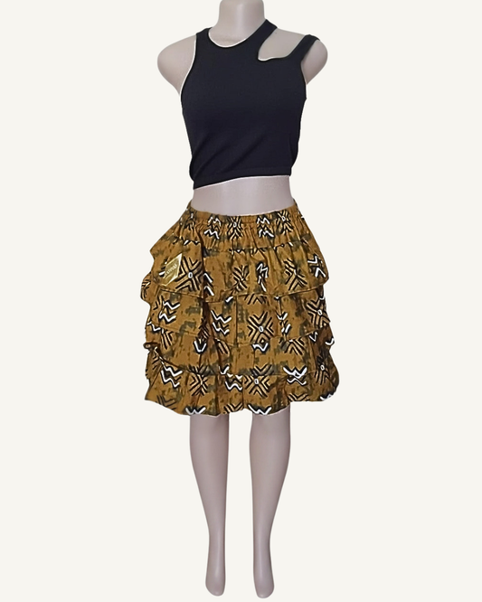 Jupe courte style bogolan à trois volants étagés froncés · fond ocre moutarde · symboles géométriques noirs et blancs étoiles croix et zigzags · taille élastiquée · longueur genou · portée avec crop top noir (couleur non choisissable à la commande).
