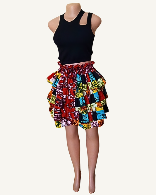Jupe courte grand patchwork wax africain à trois volants étagés froncés · multiples tissus bordeaux à motifs floraux · turquoise et noir géométrique · jaune vert batik · orange et blanc · taille élastiquée · longueur genou · portée avec crop top noir (couleur non choisissable à la commande).