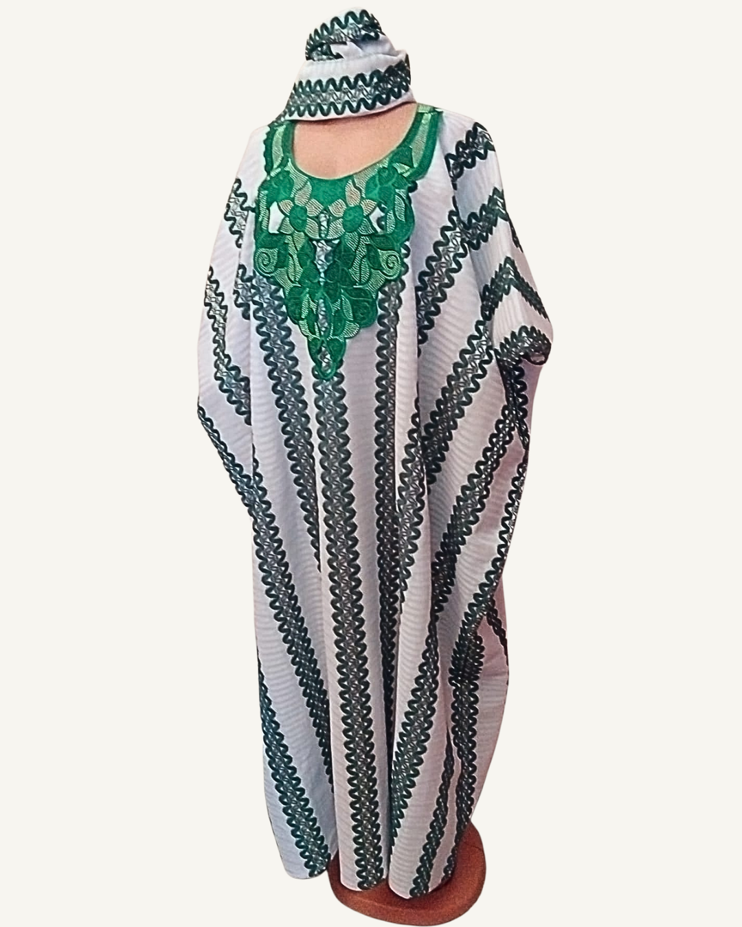 Ensemble boubou long blanc à micro-rayures, larges bandes verticales brodées vert sapin festonné de l'épaule à l'ourlet, plastron central brodé vert émeraude aux motifs floraux et feuilles entrelacées rehaussés de fils dorés, col arrondi échancré, emmanchures larges sans manches, coupe caftan ample longueur cheville, foulard assorti bordé vert noué en tête.