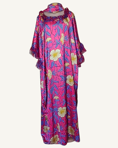Boubou long fuchsia intense · grandes fleurs hibiscus crème et jaune doré · feuilles bleu lavande · col cheminée froncé volant organza aubergine · manches trois-quarts cloche évasées à volant · coupe caftan ample longueur cheville · foulard assorti noué en tête.