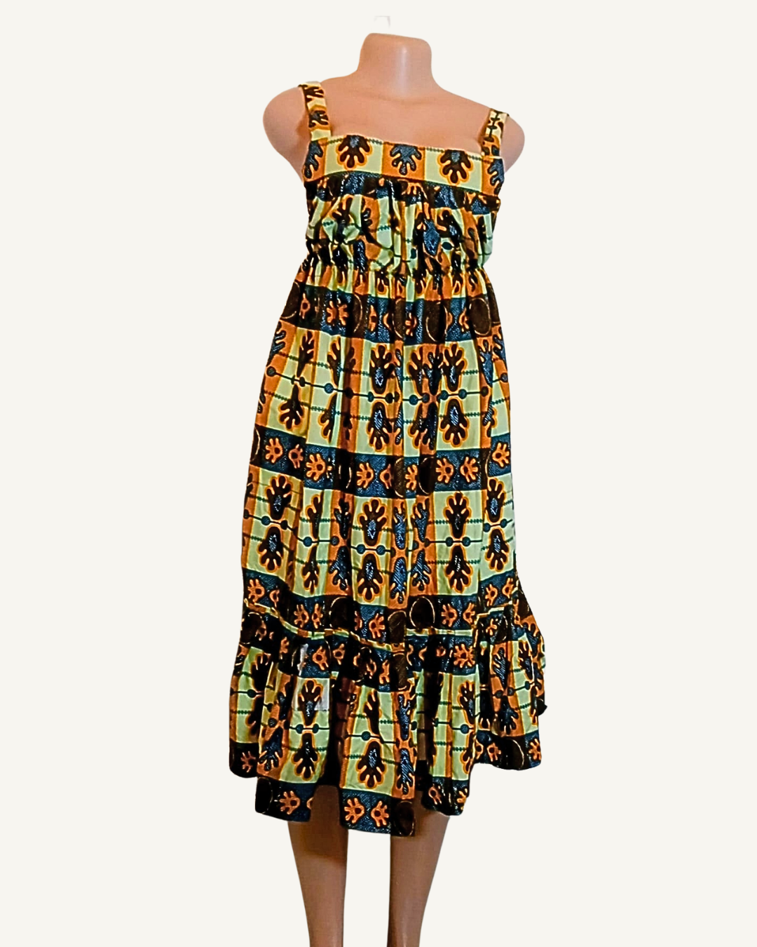 Robe wax à motifs africains en damier ocre doré, vert menthe et noir, symboles floraux répétés en miroir, encolure carrée, bretelles larges, buste élastiqué, volant bas, longueur mi-mollet · exemplaire unique Giwax Boutique.