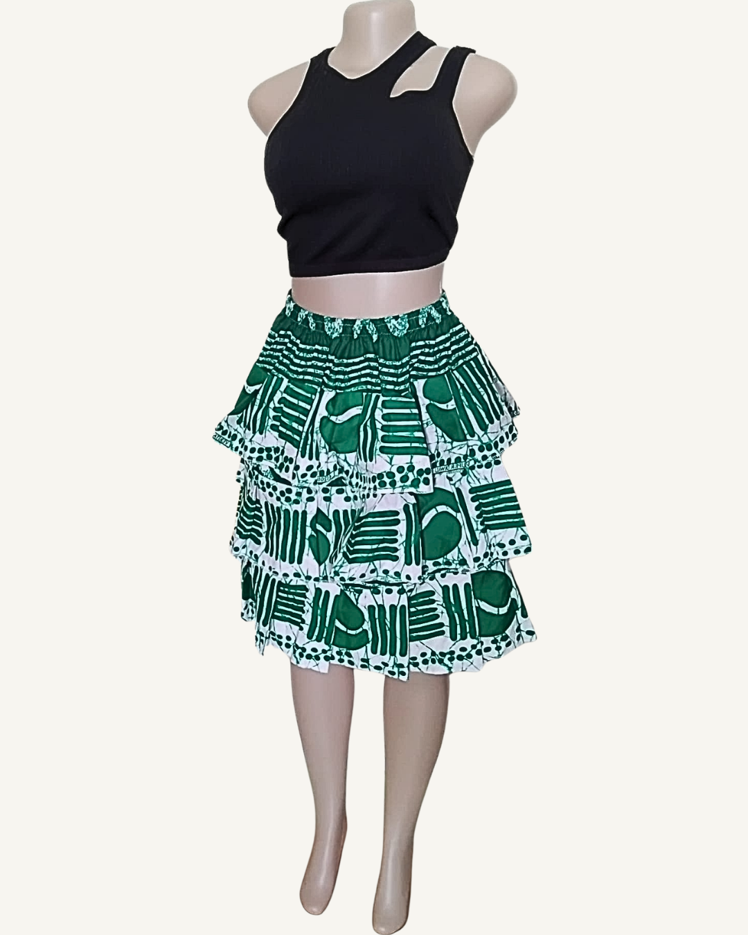 Jupe courte à trois volants étagés froncés en imprimé africain vert sapin et blanc · motifs géométriques cercles et traits · taille élastiquée · longueur genou · portée avec crop top noir (couleur non choisissable à la commande).