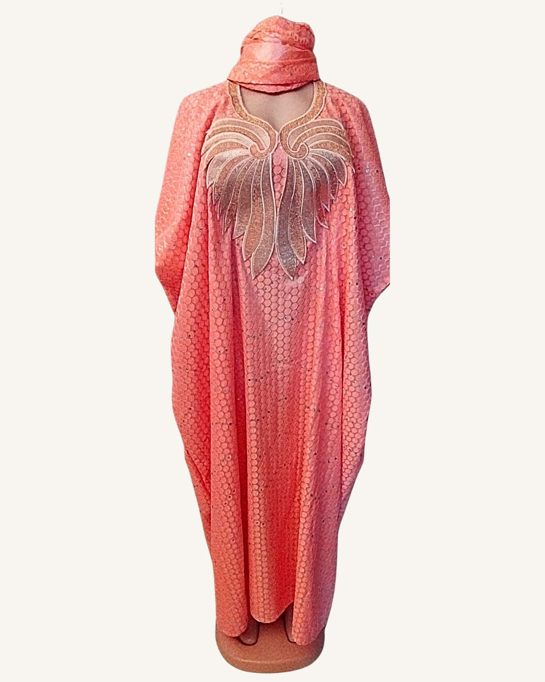 Ensemble boubou long rose saumon en bazin brodé, broderie centrale en ailes déployées fils dorés et champagne sur toute la poitrine, tissu à motifs nids d'abeille avec sequins ton sur ton, col arrondi, coupe caftan ample longueur cheville, foulard assorti noué en tête.