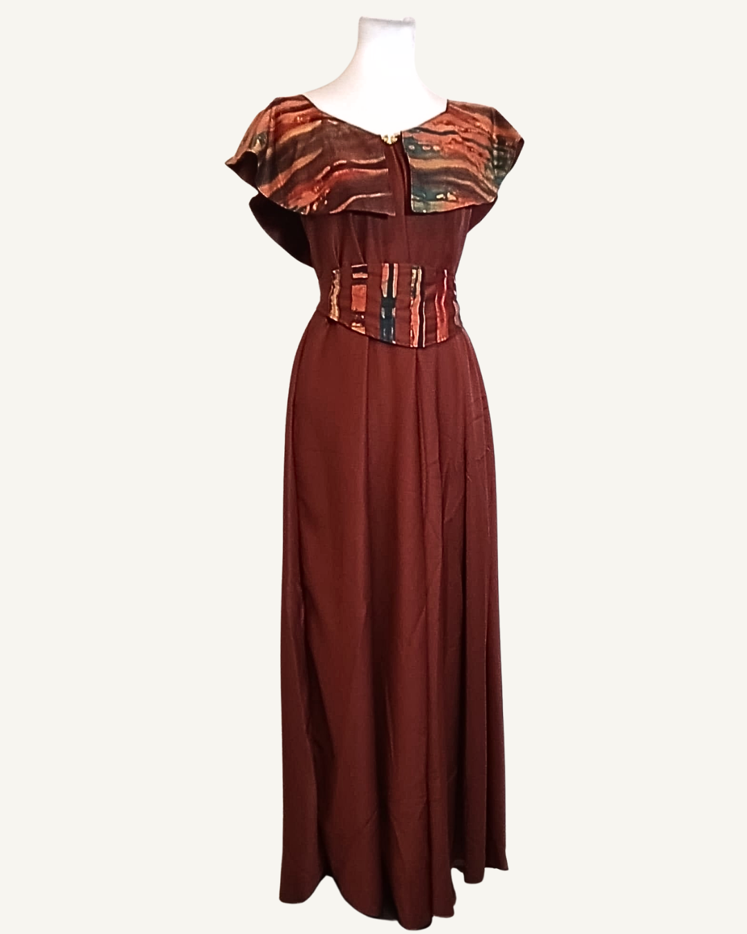 Robe longue bordeaux, cape volantée en wax cuivré aux tons ocre et dorés, corset amovible assorti à la taille, bouton doré au décolleté, jupe évasée longueur cheville · exemplaire unique Giwax Boutique.