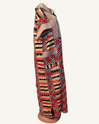 Vue de profil — robe longue batik africain patchwork rouge noir et orange, empiècement beige lin avec col chemise et zip central, manche courte batik à revers beige, poche plaquée beige visible sur le côté, coupe droite ample longueur cheville.