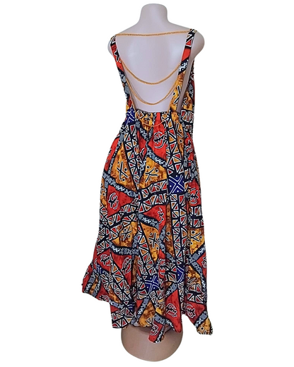 Dos nu d'une robe batik multicolore avec chaîne dorée cousue traversant le dos d'une bretelle à l'autre · motifs africains graphiques · ourlet asymétrique.