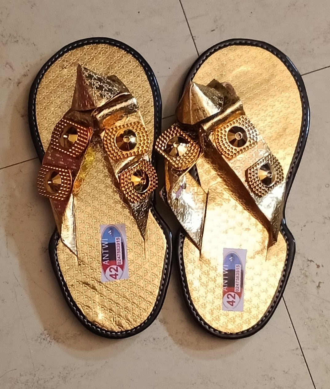 Agbodje dorées traditionnelles ivoiriennes portées · bride en V métallisée or · médaillon central doré · semelle gaufrée or · contour noir · vue de dessus.