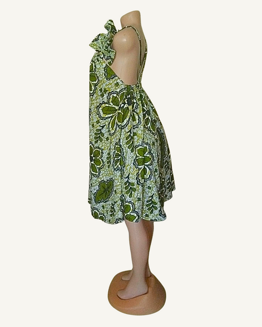 Robe wax verte, coupe évasée, ourlet asymétrique tombant en pointe, profil montrant le dos nu et le tombé généreux de la jupe.