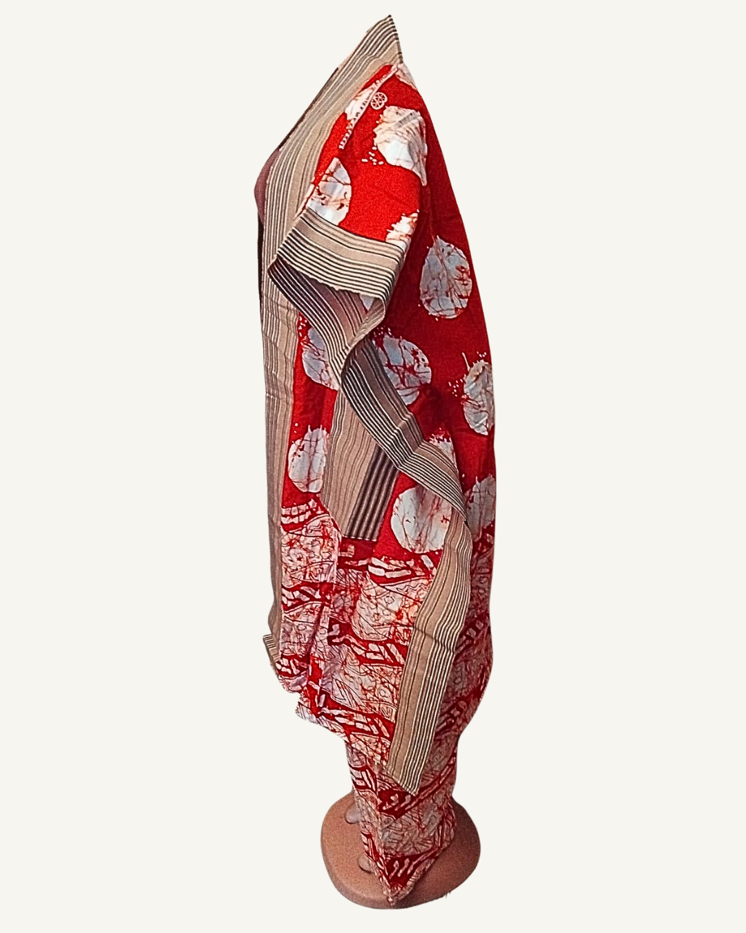 Vue de profil — silhouette de l'ensemble kimono ouvert sur le pantalon coordonné, tombé des manches larges, bordure rayée beige visible sur l'ourlet et la cheville du pantalon, tissu batik rouge à cercles blancs.