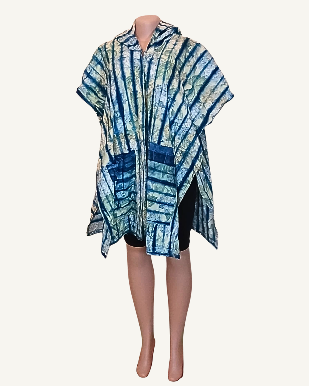 Vue face · poncho adire shibori · zip central devant · deux poches plaquées visibles · capuche · manches courtes larges · coupe ample · porté sur cycliste noir non inclus.
