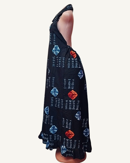 Vue de profil — robe longue adire africain noir, col chemise halter, motifs losanges concentriques bleu et rouge orangé alternés avec tirets blancs, silhouette droite et fluide jusqu'à la cheville, volant froncé en ourlet.