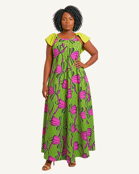 Femme portant une robe longue wax à grands motifs floraux fuchsia sur fond vert, bretelles à nœuds vert anis, volants aux épaules, buste élastiqué, coupe très évasée longueur cheville · exemplaire unique Giwax Boutique.