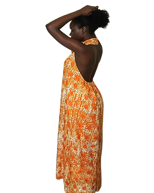 Femme portant une robe longue batik orange dos entièrement nu, col halter, coupe ample et fluide · imprimé africain motifs soleil · longueur cheville.